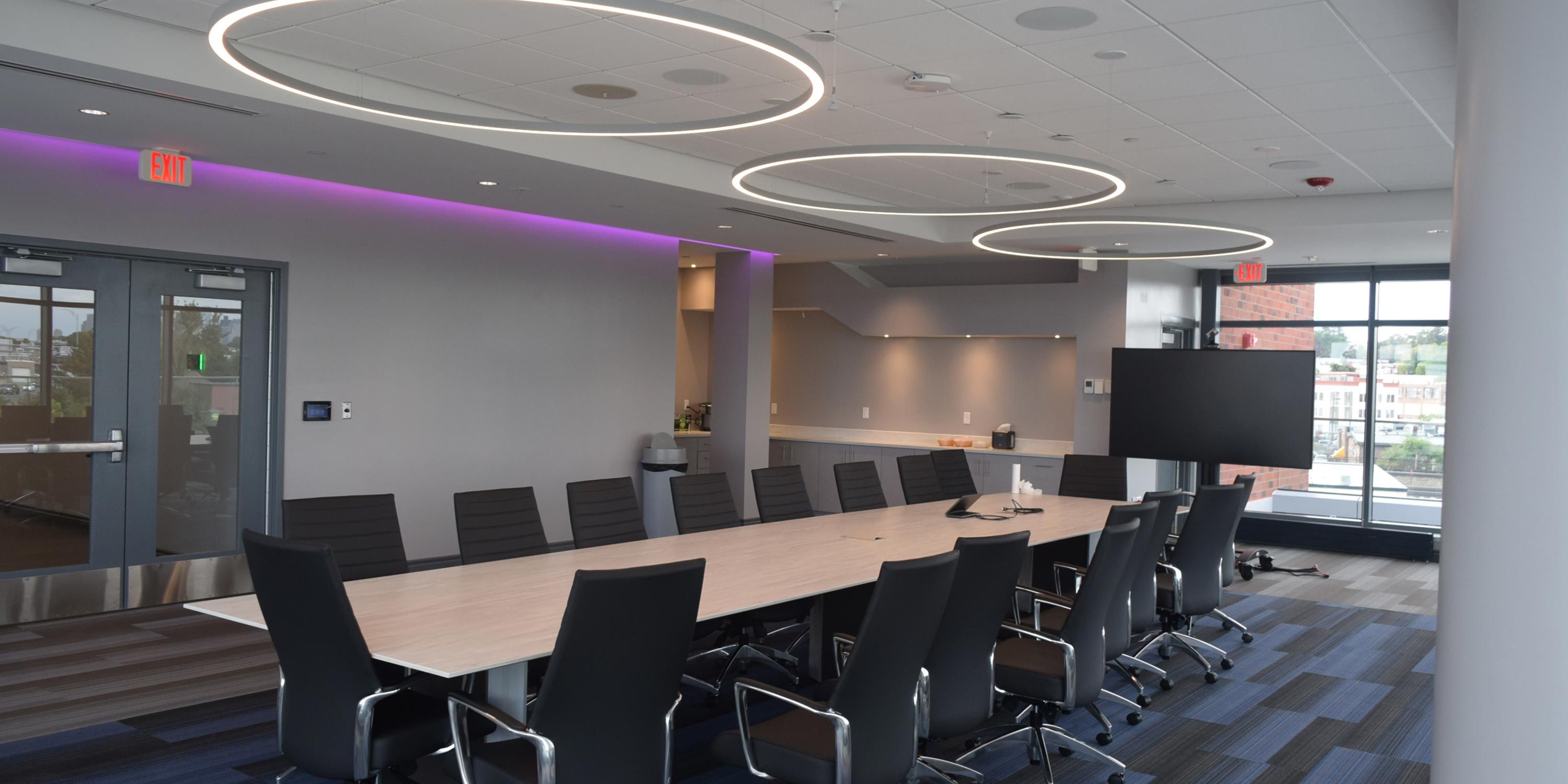 A sleek conference room with a long table, black chairs, and circular ceiling lights overhead.