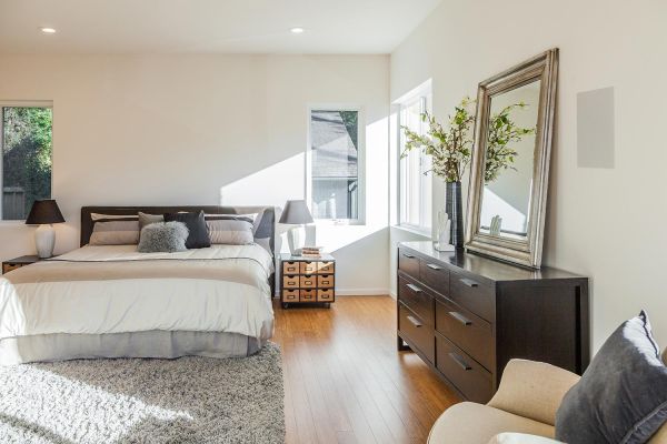 A bright and airy bedroom with a large bed, wooden dresser, and an oversized mirror, bathed in natural light.