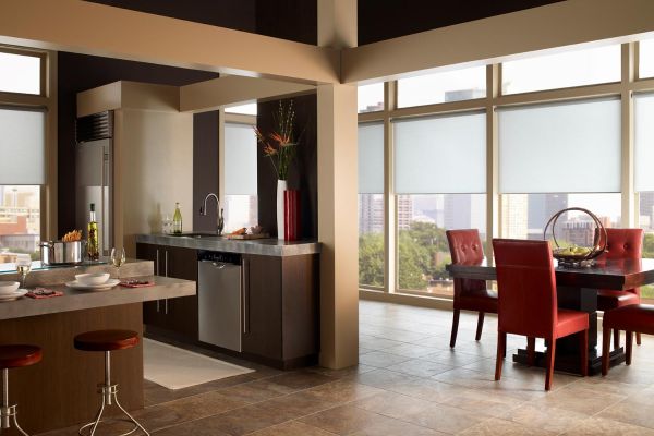 A spacious kitchen and dining area with dark cabinets, red dining chairs, and large windows offering city views, creating a warm, urban ambiance.