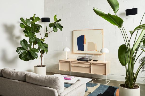 A contemporary living area with light decor, large potted plants, and a stylish console holding a record player beneath abstract wall art.