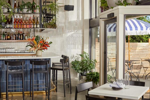 A trendy bar with high seating, vibrant plants, and a chic, tiled counter, blending indoor and outdoor elements seamlessly.