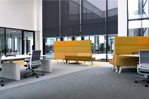 An open office space with modern workstations, high-backed seating for privacy, and large windows with black shades.