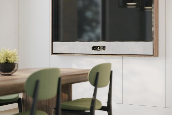 A small meeting room with a mounted display, green chairs, and pendant lighting over a wooden table.