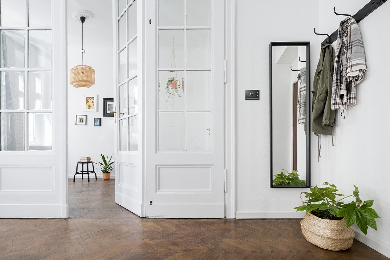 A bright, modern entryway with white French doors, a hanging woven light fixture, and a smart thermostat on the wall.