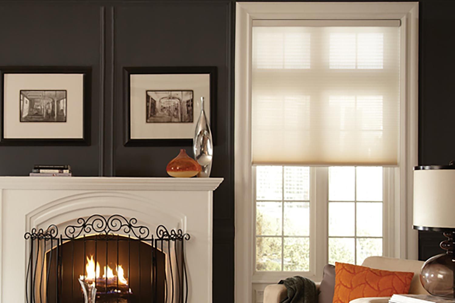 A cozy living area with dark walls, a white fireplace, and cellular shades filtering soft light through the windows, creating a warm atmosphere.