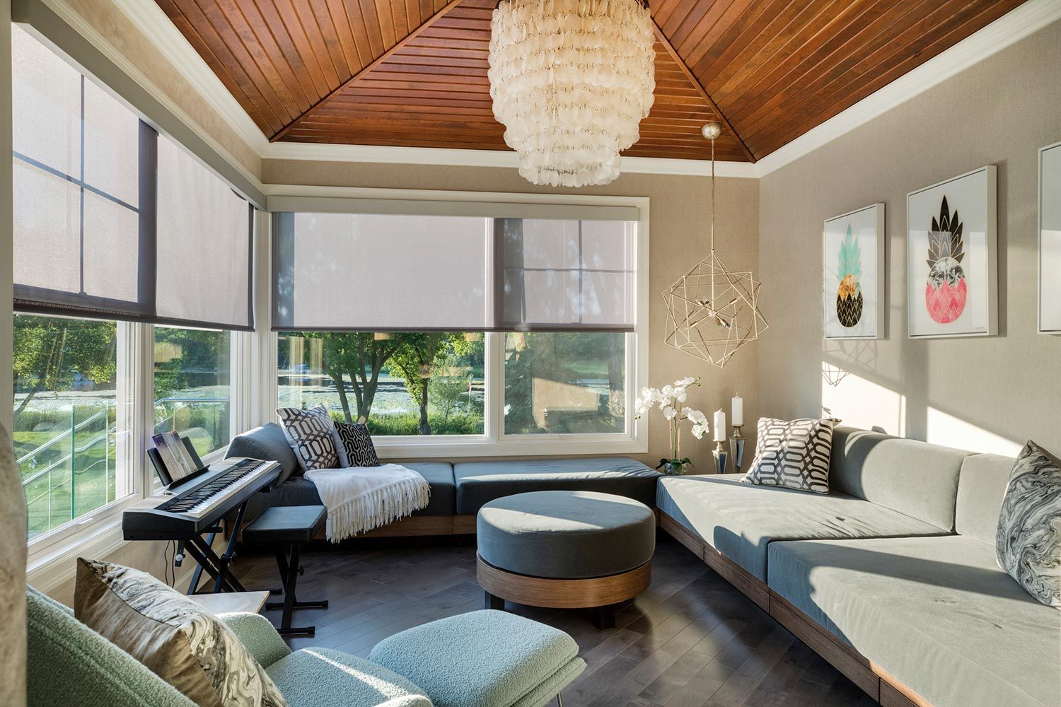 A sunlit room with motorized window shades, comfortable seating, and a piano near large windows overlooking a serene outdoor view.